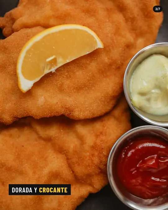 Bodegón La Esquina, lámina 3 de 7: Primer plano de milanesas doradas con una rodaja de limón y potecitos de salsas.
