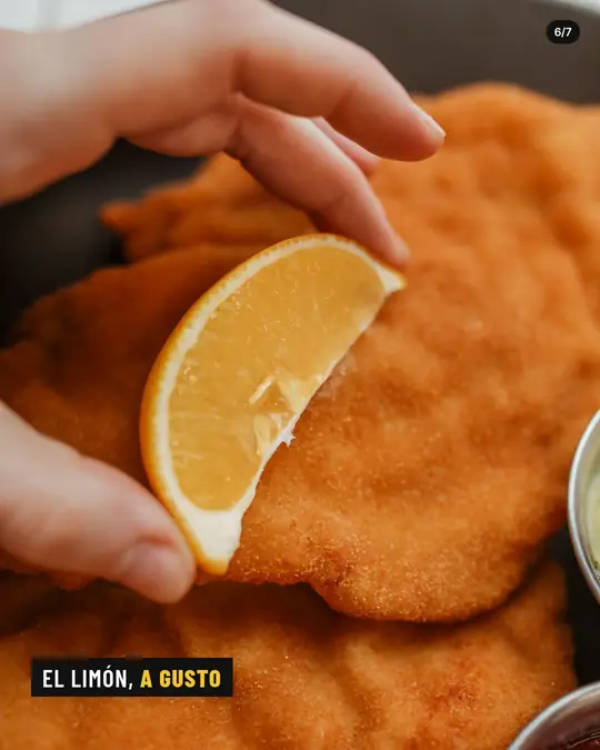 Bodegón La Esquina, lámina 6 de 7: Dedos que exprimen una rodaja de limón sobre la milanesa, muy de cerca.