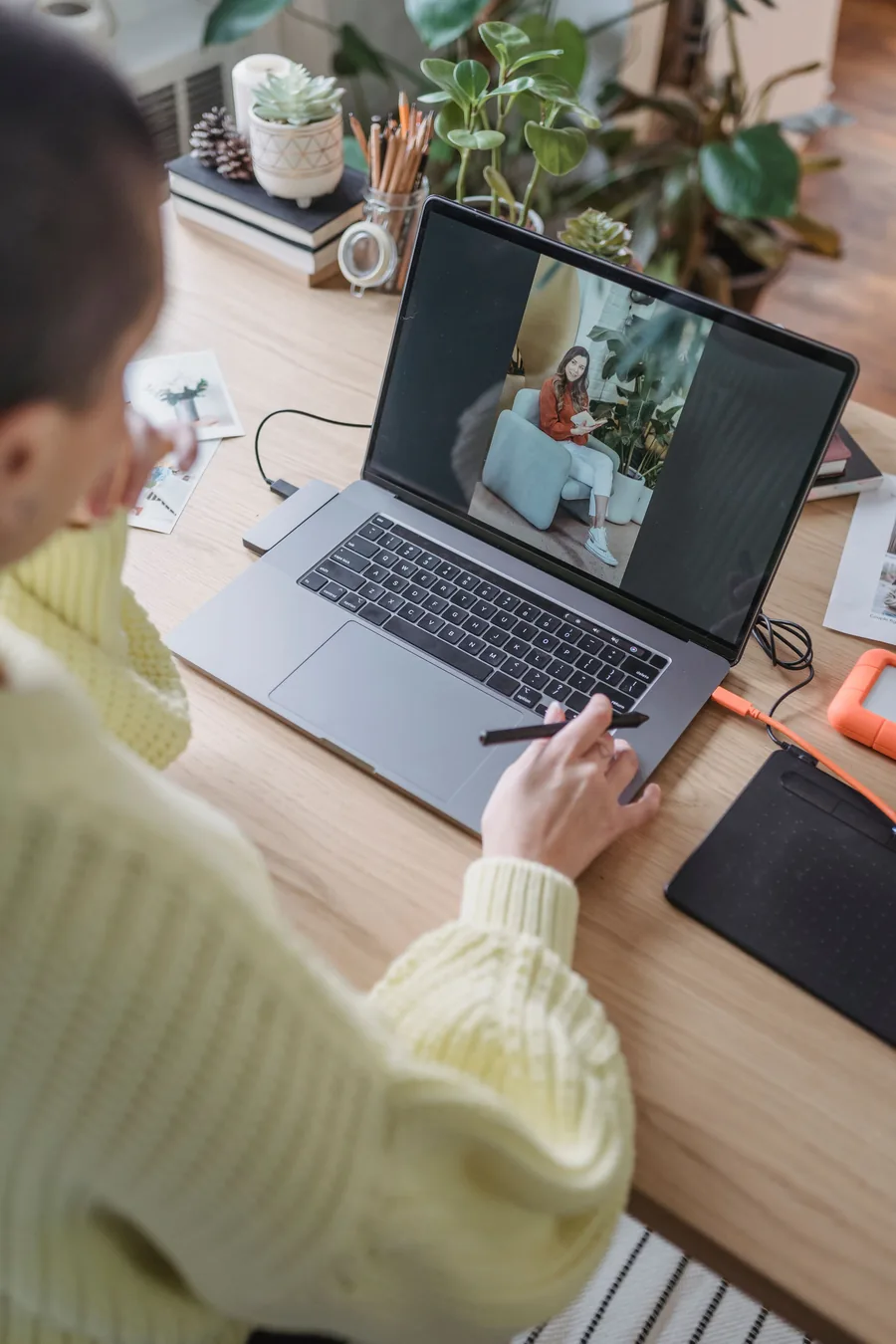 Mujer retoca una foto en su laptop con un lápiz digital; al lado, una tableta gráfica y un disco externo naranja