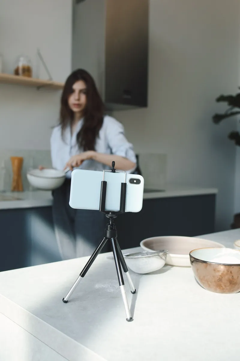 Mujer se graba con el celular en un trípode mientras cocina, en su cocina